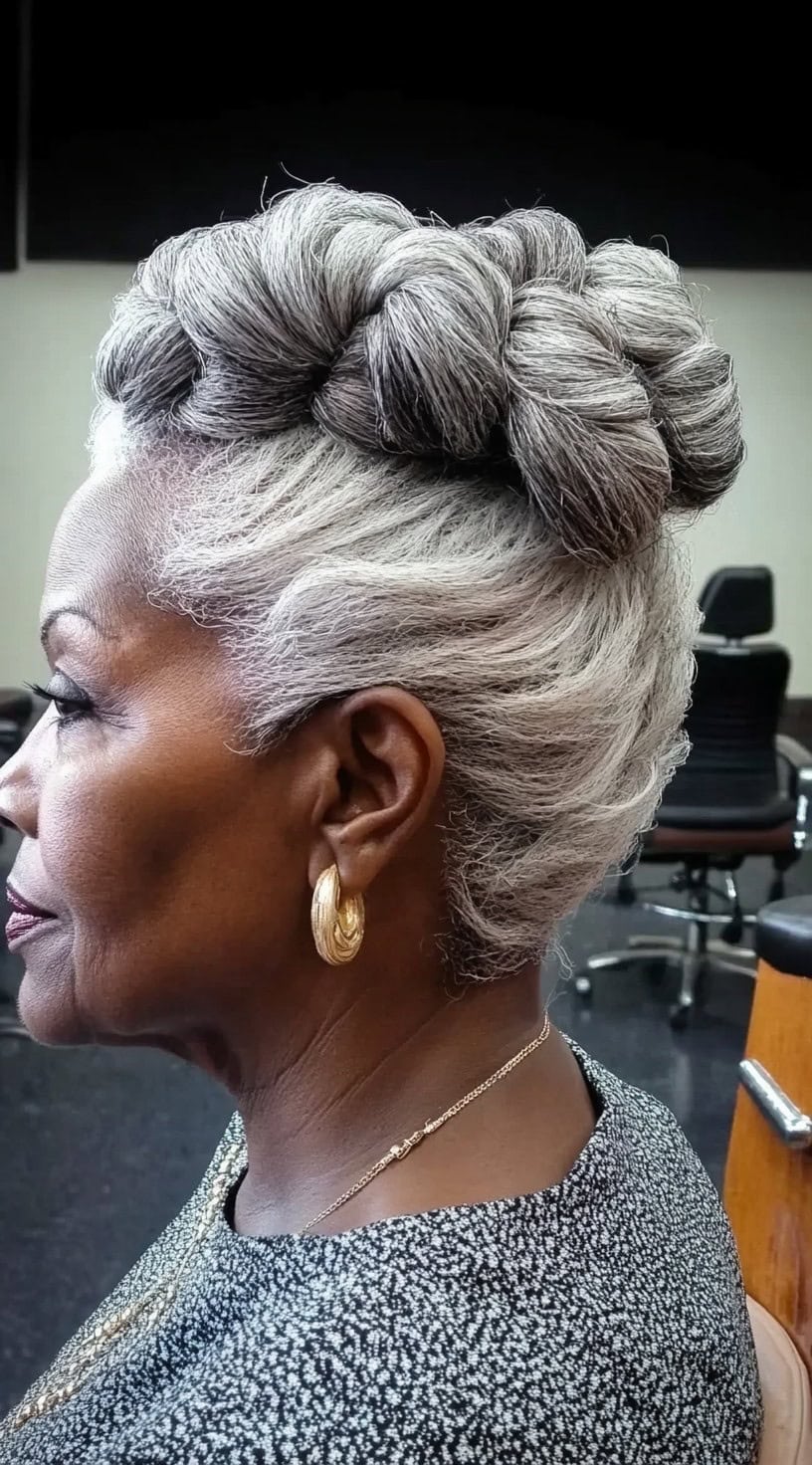 A side view of an older black woman with natural gray hair styled into an elegant, thickly twisted crown updo.