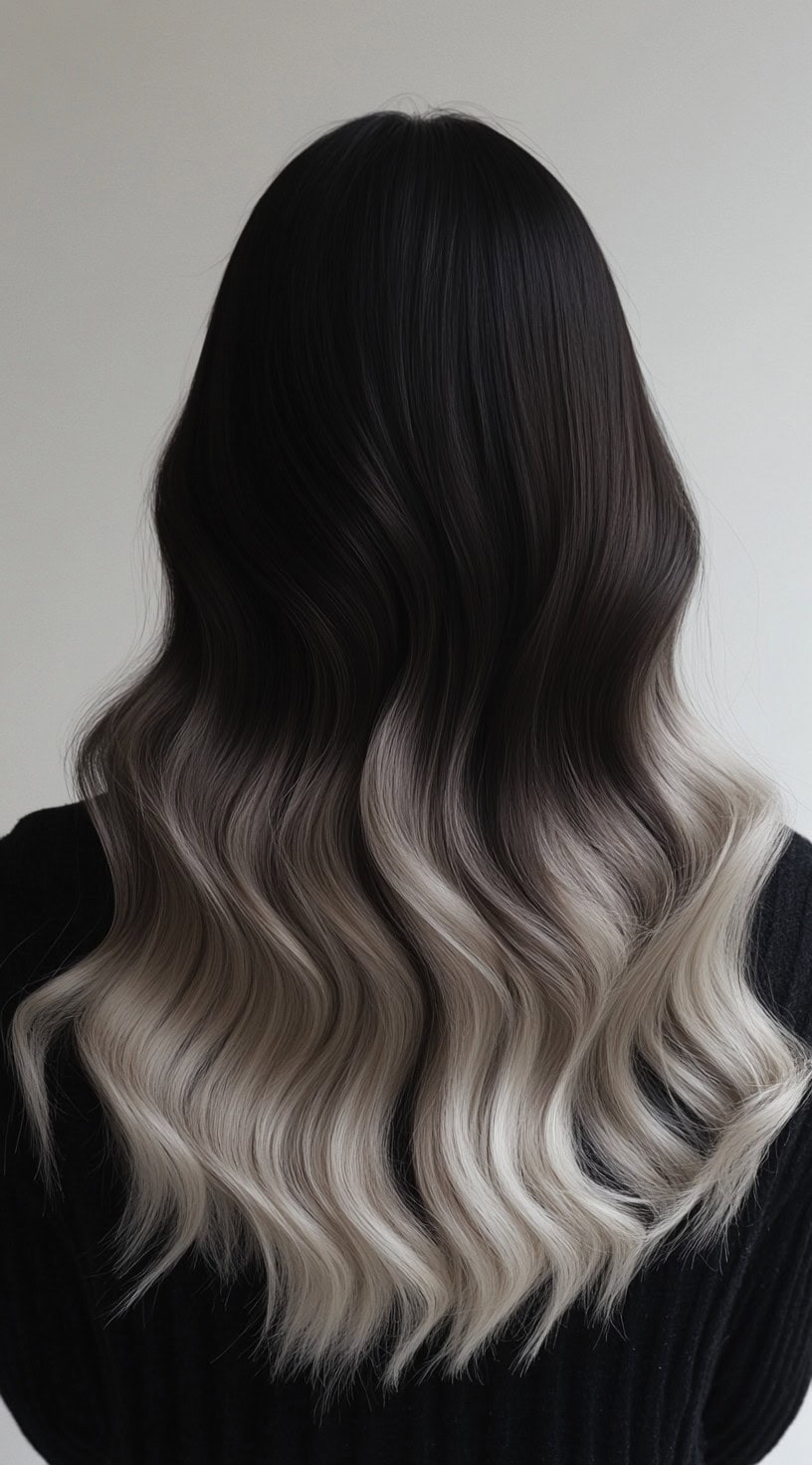A long wavy hairstyle with dark brown roots fading into ash blonde balayage