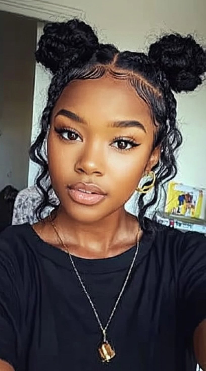 A woman with thick, braided space buns styled in a middle part, with delicate tendrils and neatly laid baby hairs.
