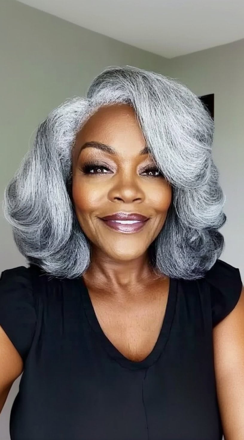 A joyful older Black woman with a layered silver bob styled with a soft flip, wearing a fitted black blouse and a radiant smile.