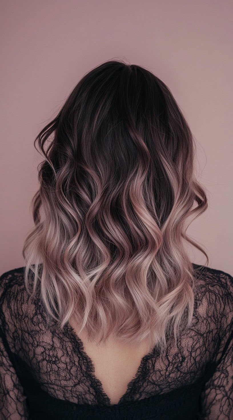 A back view of a wavy, shoulder-length hairstyle with dark berry roots transitioning into muted strawberry blonde and soft rose gold ends.
