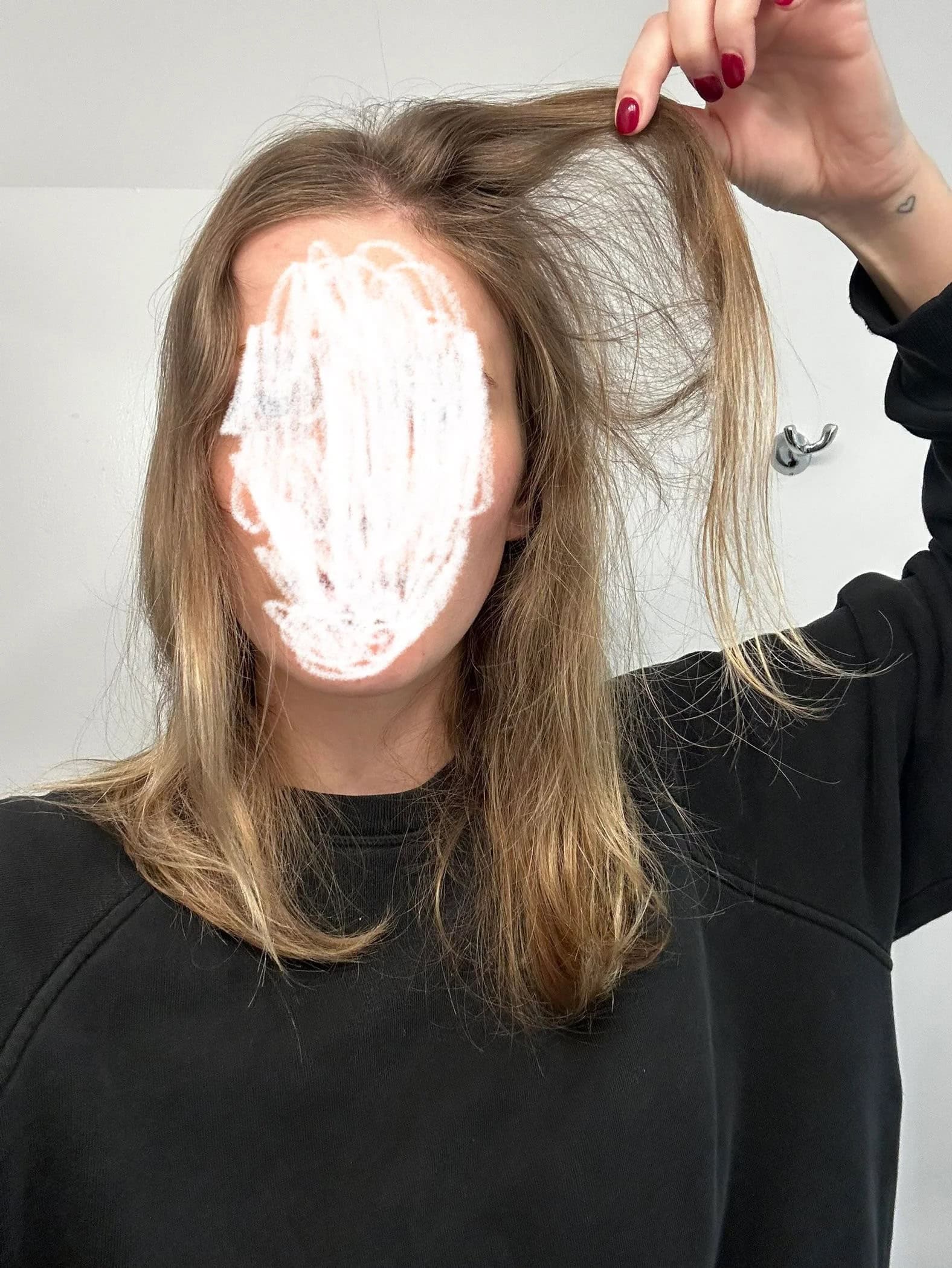 Close-up of fine blonde hair being lifted by hand, revealing the thin and flat texture at the roots.