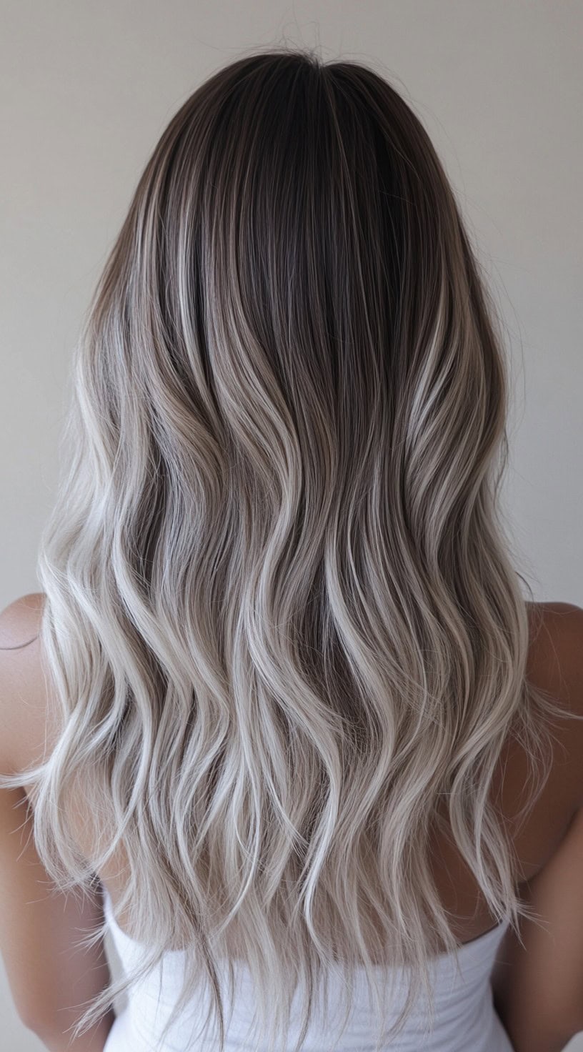 Long wavy hair with dark roots blending into ash blonde tones.