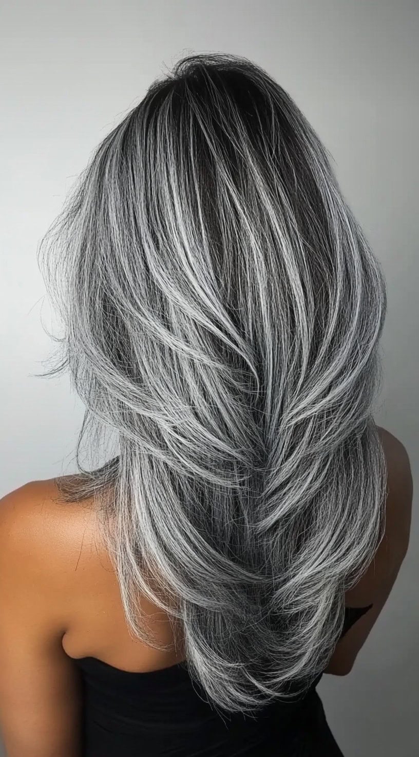 A woman with long, silver-toned feathered layers styled in soft waves for an elegant and sophisticated look.
