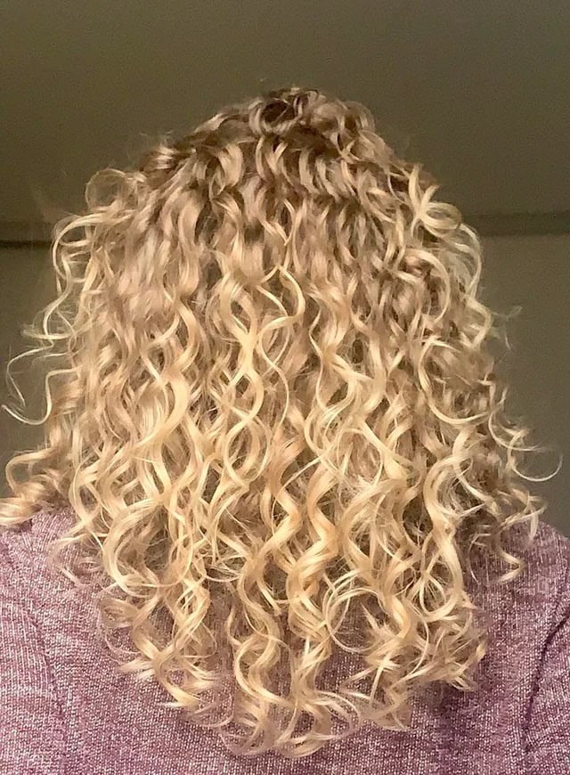 Thin blonde hair with tight, defined curls styled for maximum volume and shape retention.