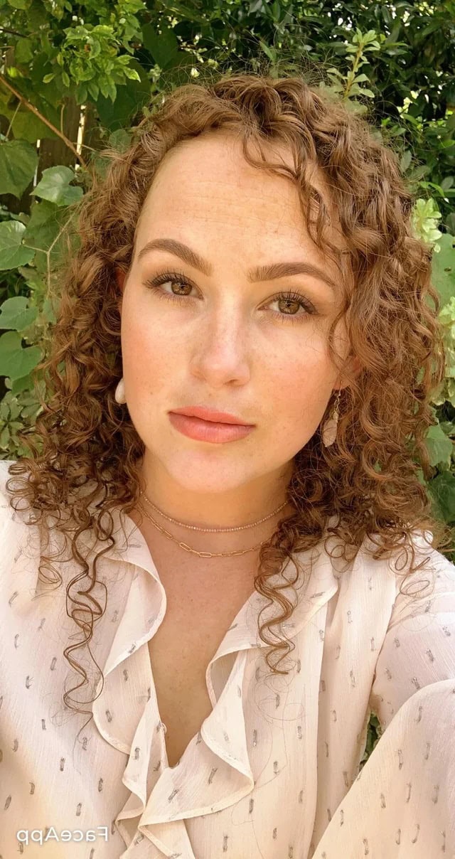 Woman with fine, tight natural curls wearing a light blouse, showcasing defined curl texture in daylight.