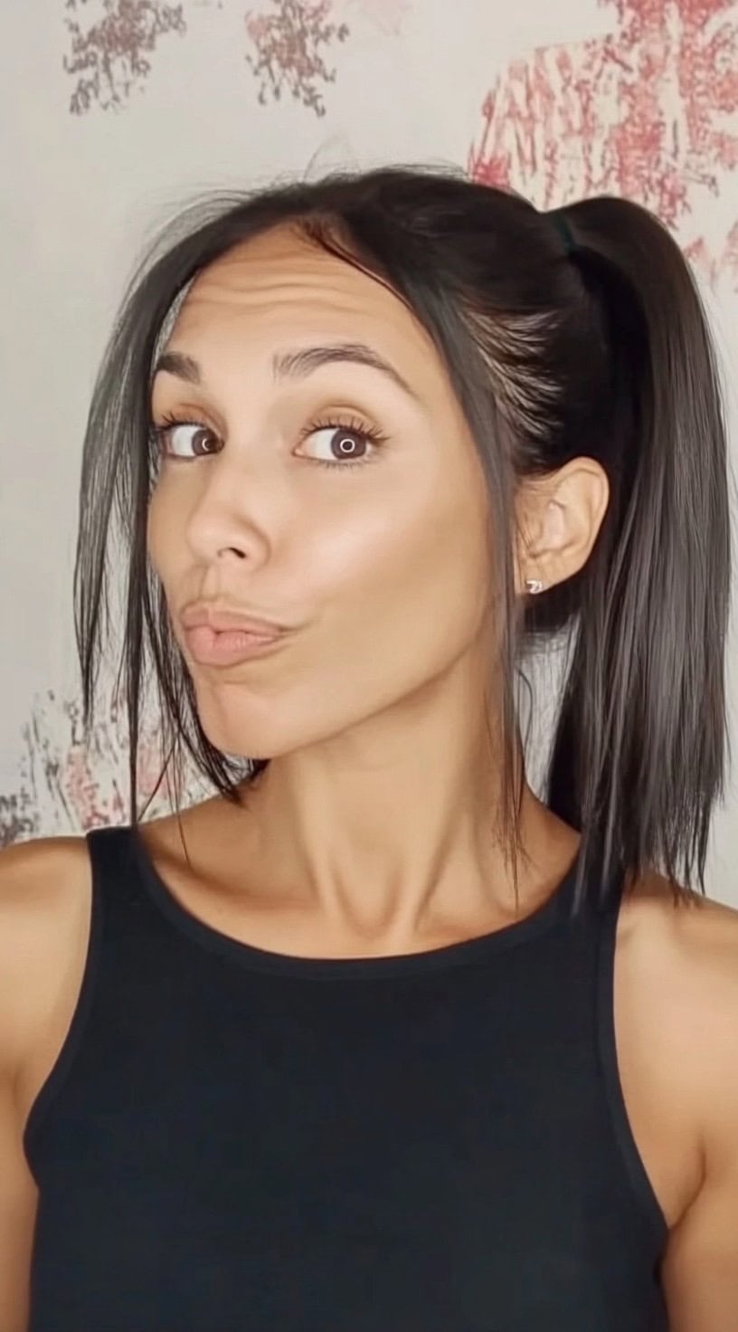 Woman with dark straight hair styled in a high ponytail, with long face-framing strands left loose for softness.