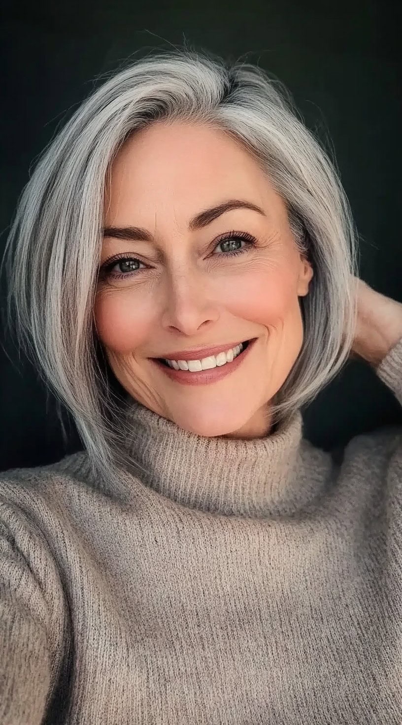 A woman with a sharply angled A-line bob and a deep side sweep, showcasing grey-blonde hair with smooth shine.