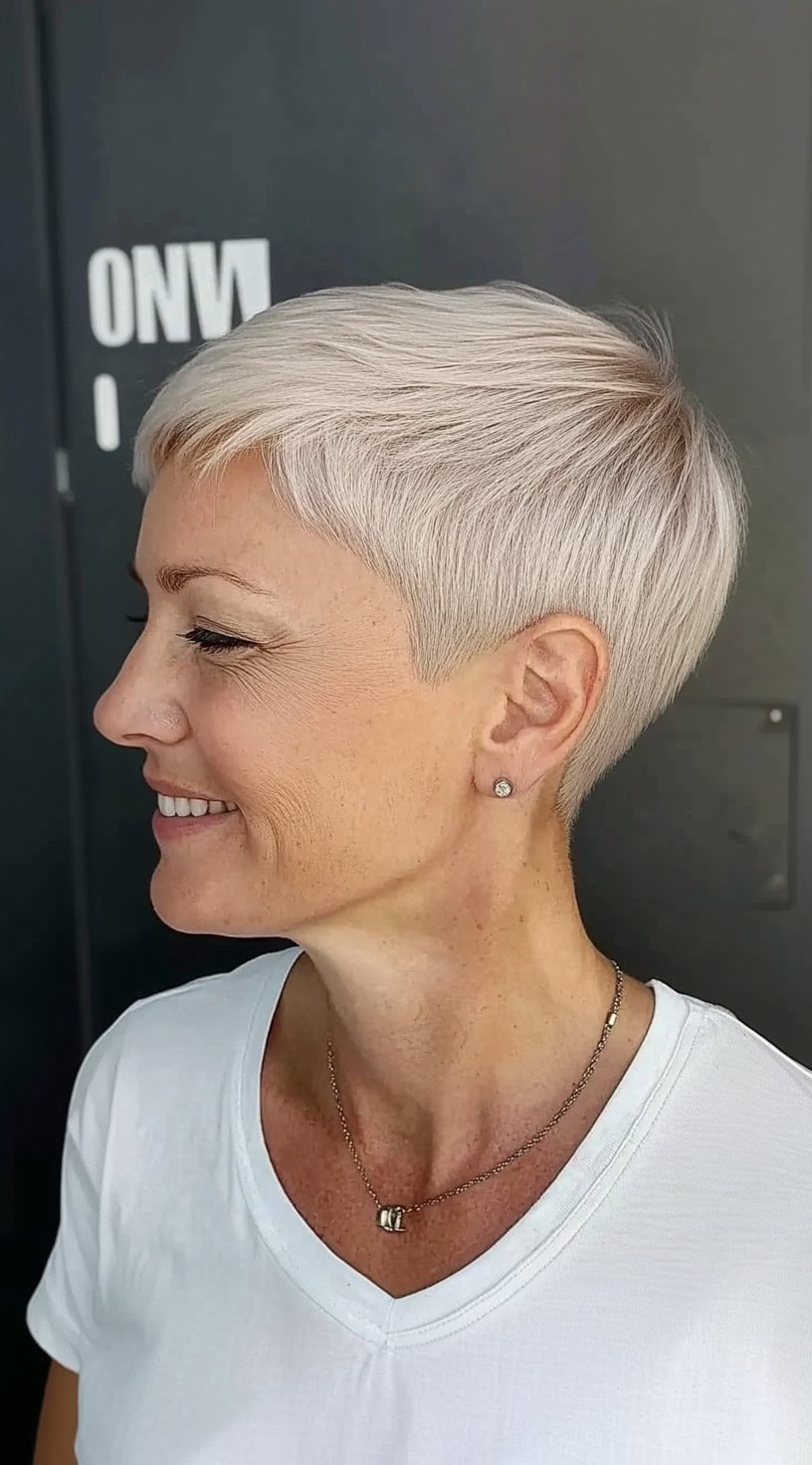 A close-cropped platinum hairstyle with micro layers and a soft taper toward the nape, styled with clean lines and shine.