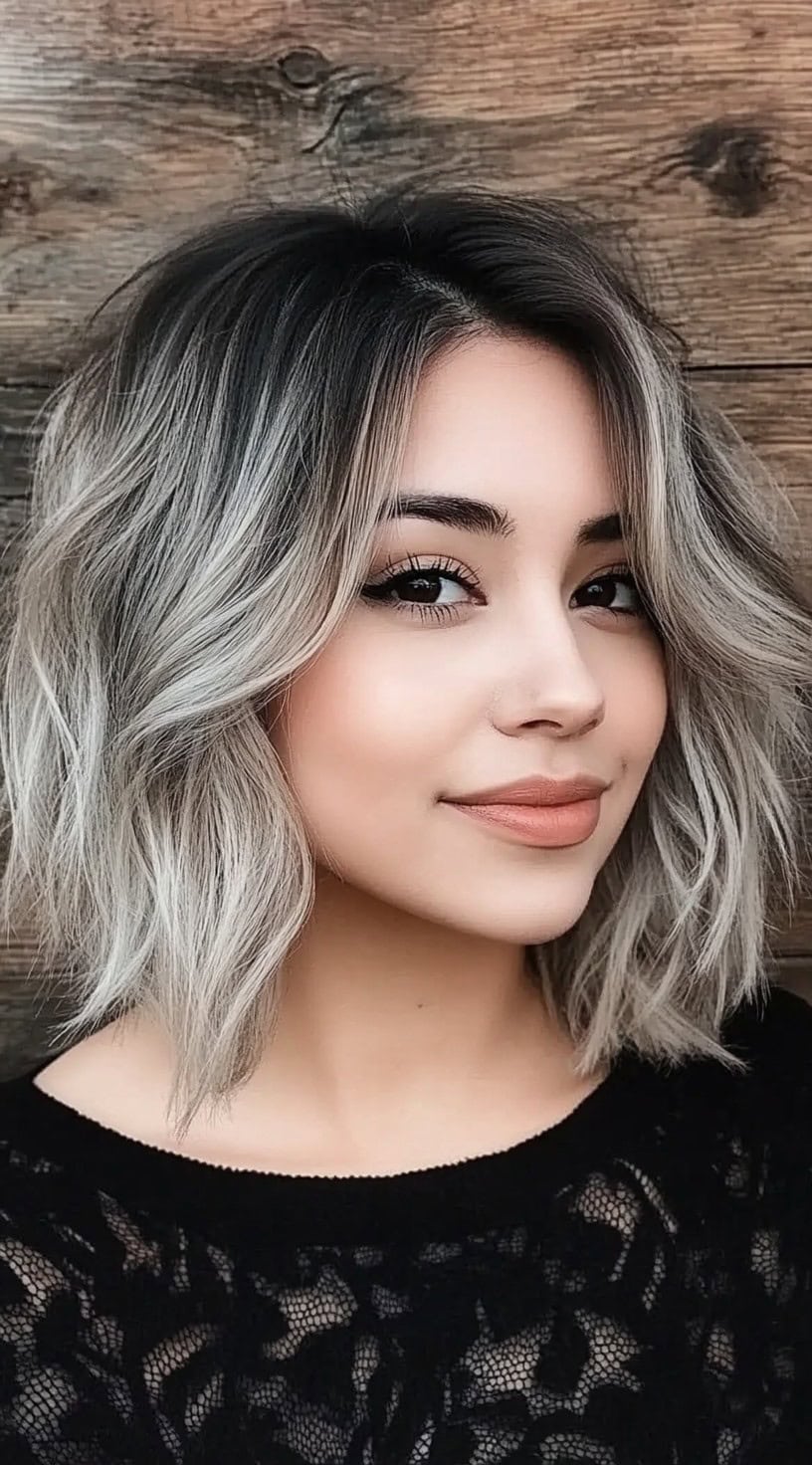 A woman with a smoky silver shag bob, featuring a dark shadow root and soft tousled waves.