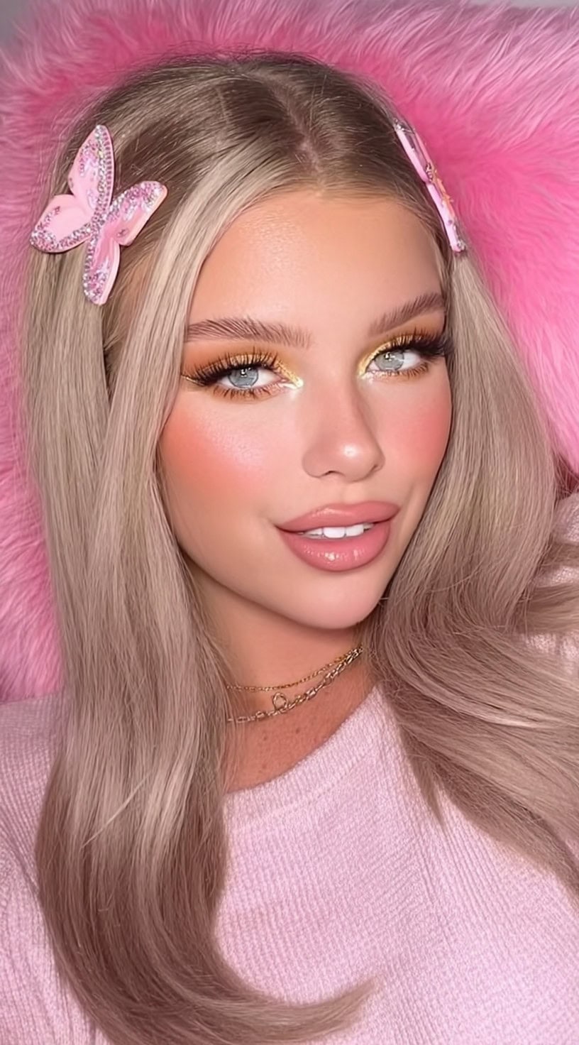 A woman with long, sleek blonde hair parted down the middle, accessorized with pink rhinestone butterfly clips on each side.
