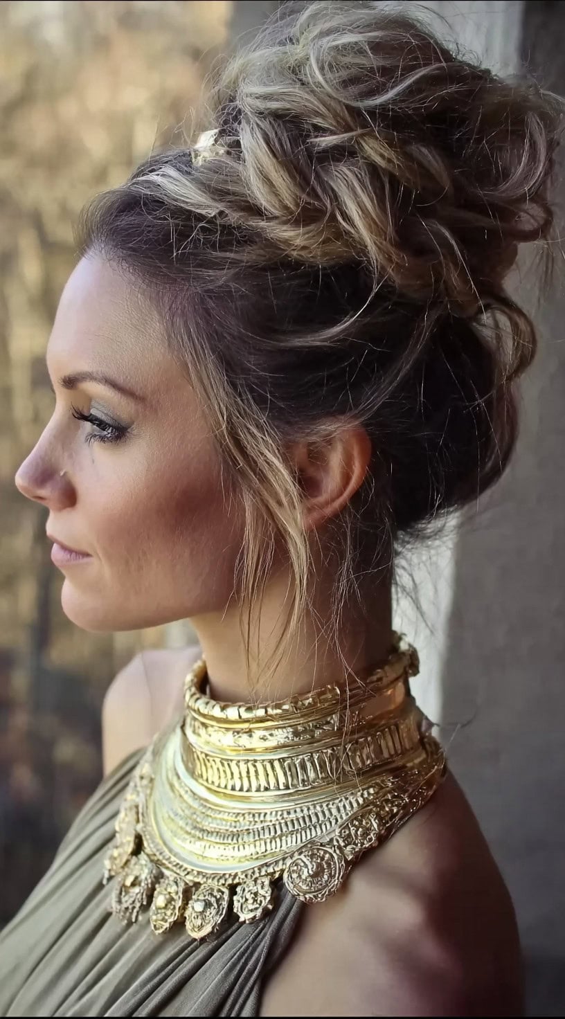Side view of a woman with a softly textured updo featuring twisted sections and loose strands framing the face.