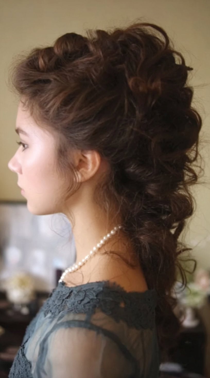 Profile view of a woman with long, voluminous Victorian curls styled down the back with height at the crown.