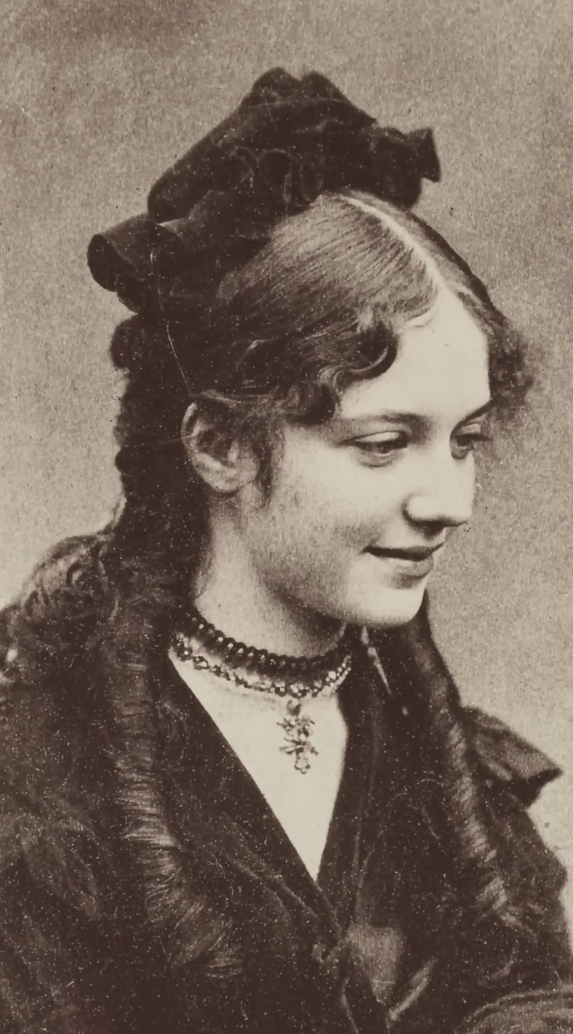 Vintage photograph of a young woman with curled hair half-up, decorated with a ribbon bow.